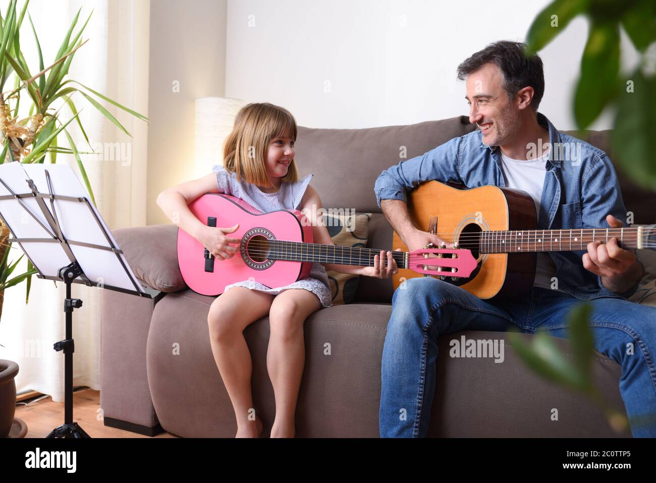 Father and daughter playing guitar in the living room looking at each other smiling with complicity Stock Photo