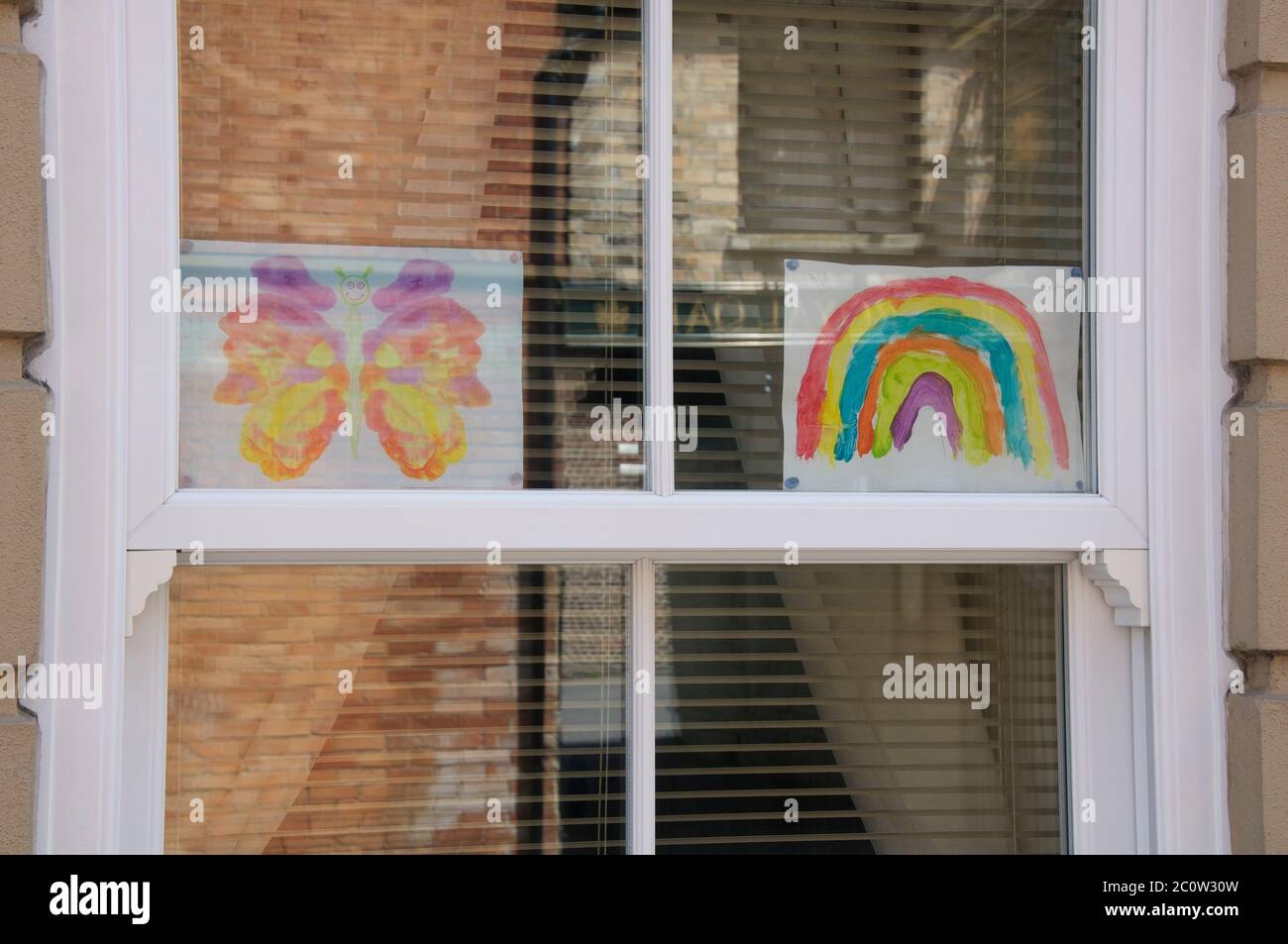 Children’s drawings of a rainbow and a butterfly, with the message “Stay safe”, displayed in the window of a house. The Coronavirus pandemic. England. Stock Photo