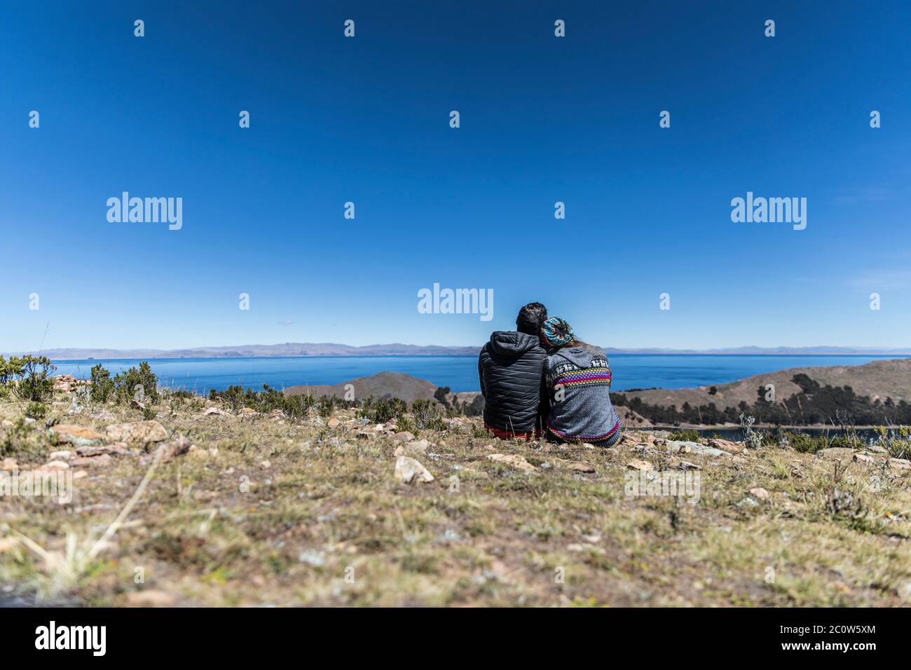 couple resting in a hill by a huge lake in bolivia Stock Photo