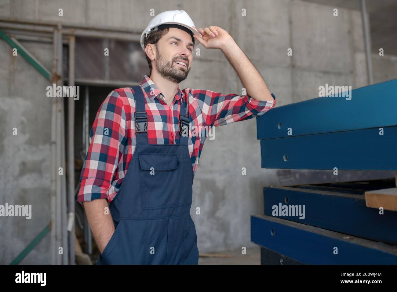 Building worker in helmet and checked shirt standing with one hand in