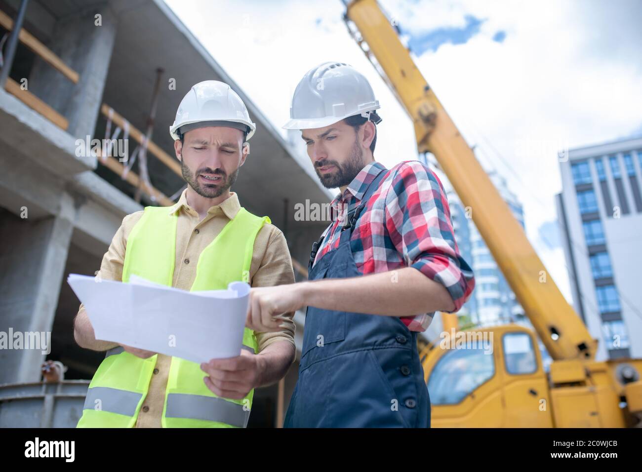 Building workers.standing in front of crane, checking blueprint Stock ...