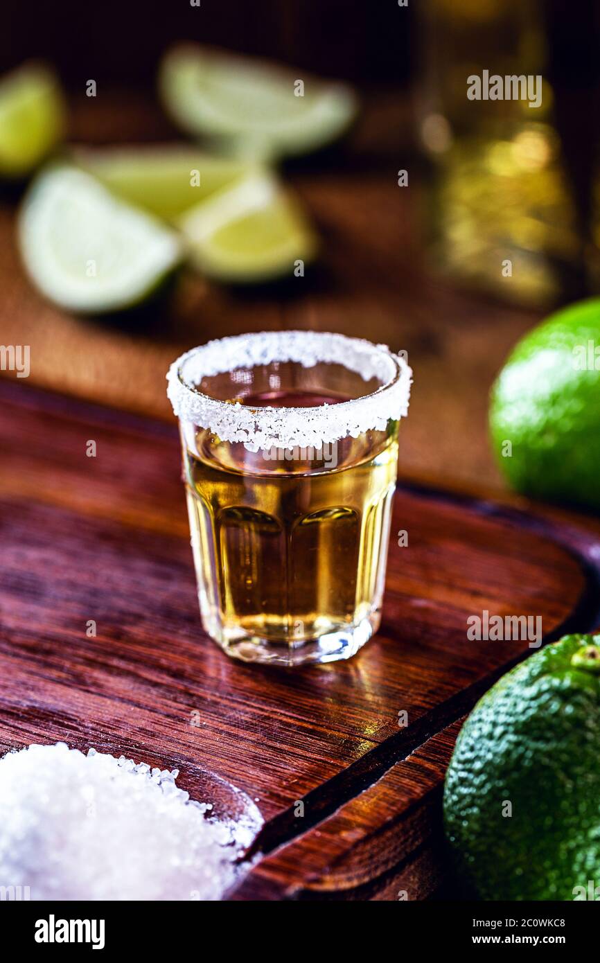 glass of tequila, on wooden table, with lemons and salt in the background.  fiery drink with vodka Stock Photo - Alamy