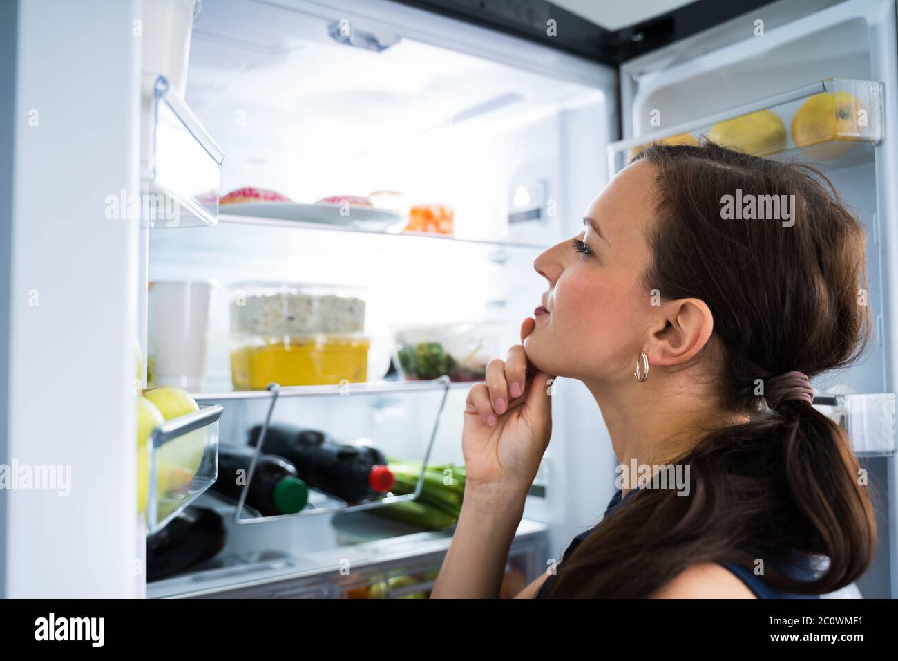 Hungry Woman Looking For Food In Kitchen At Home Stock Photo