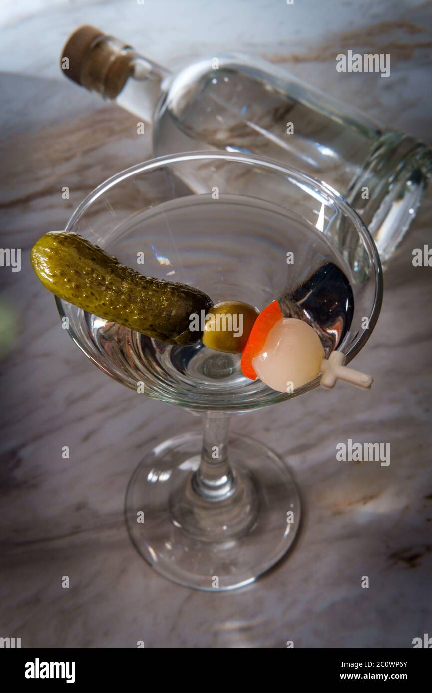 Dry gin martini served neat with pickle cocktail stirrer and bottle in background Stock Photo