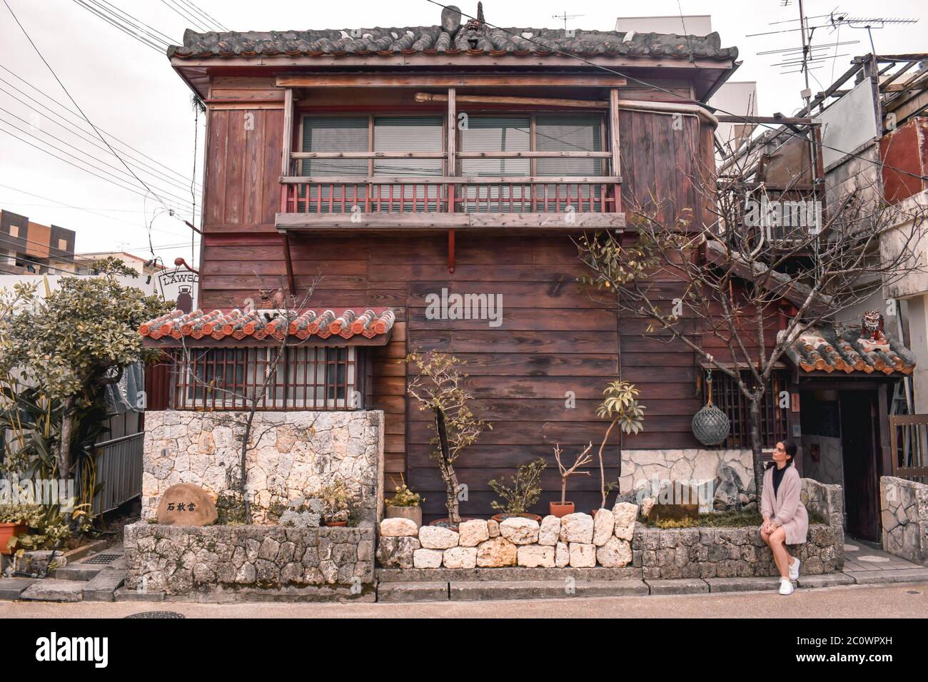 Girl sitting in front of a traditional Japanese wooden house in Naha Okinawa Japan Stock Photo
