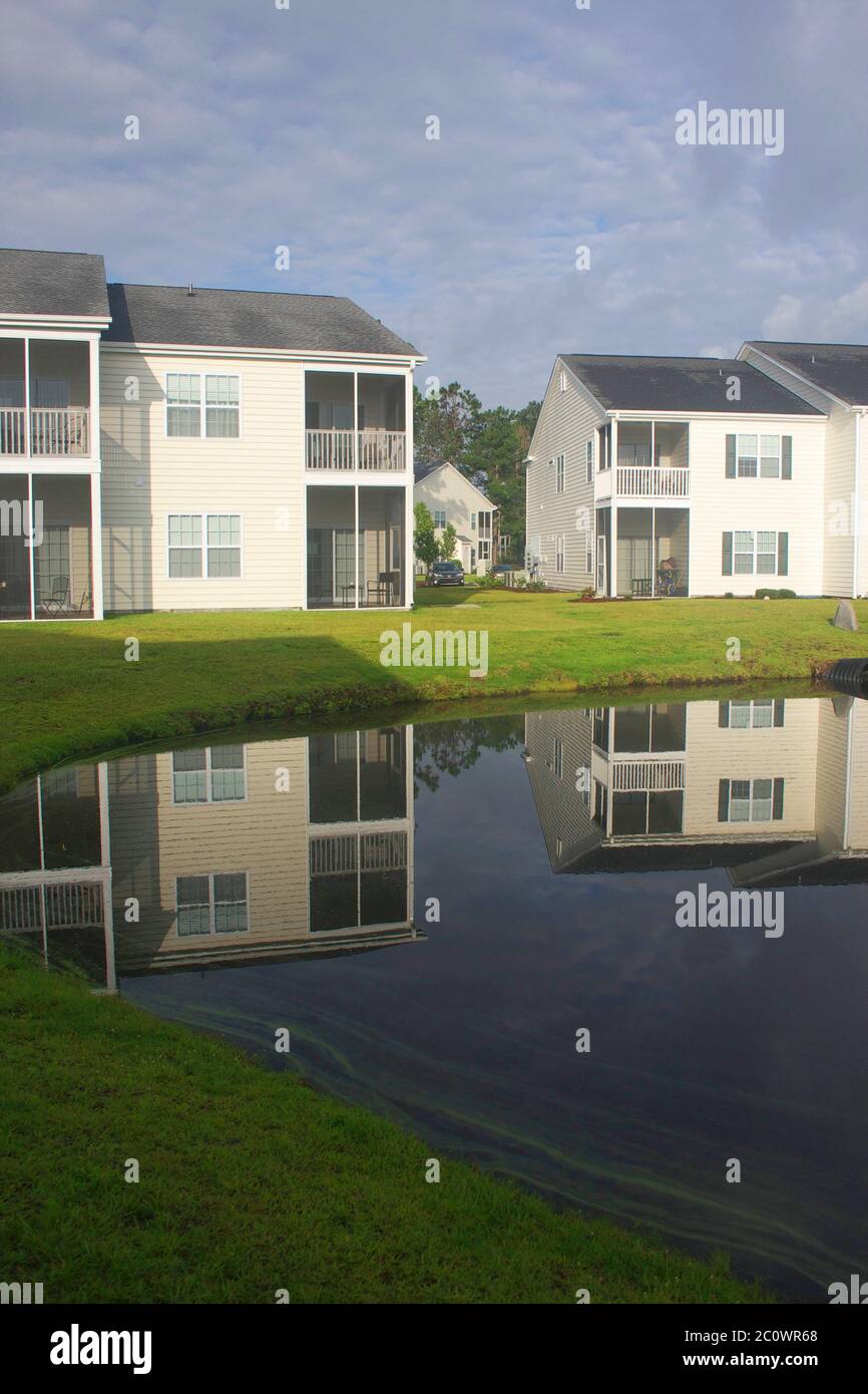 Background with a modern neighborhood with buildings around the pond. Houses reflected in the tranquil water during beautiful cloudy morning. Vertical Stock Photo