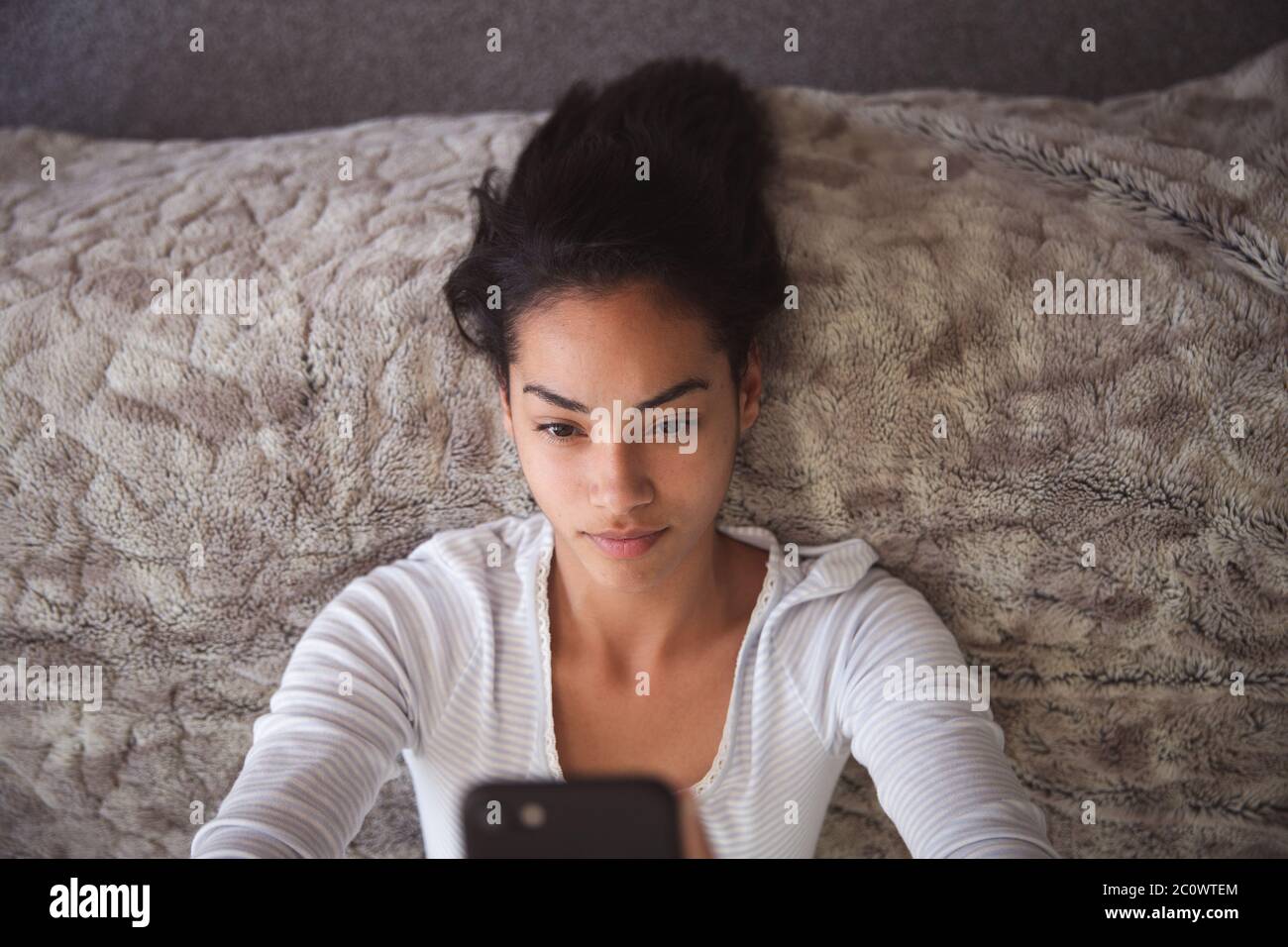 Mixed race woman using smartphone on bed during coronavirus covid19 pandemic Stock Photo