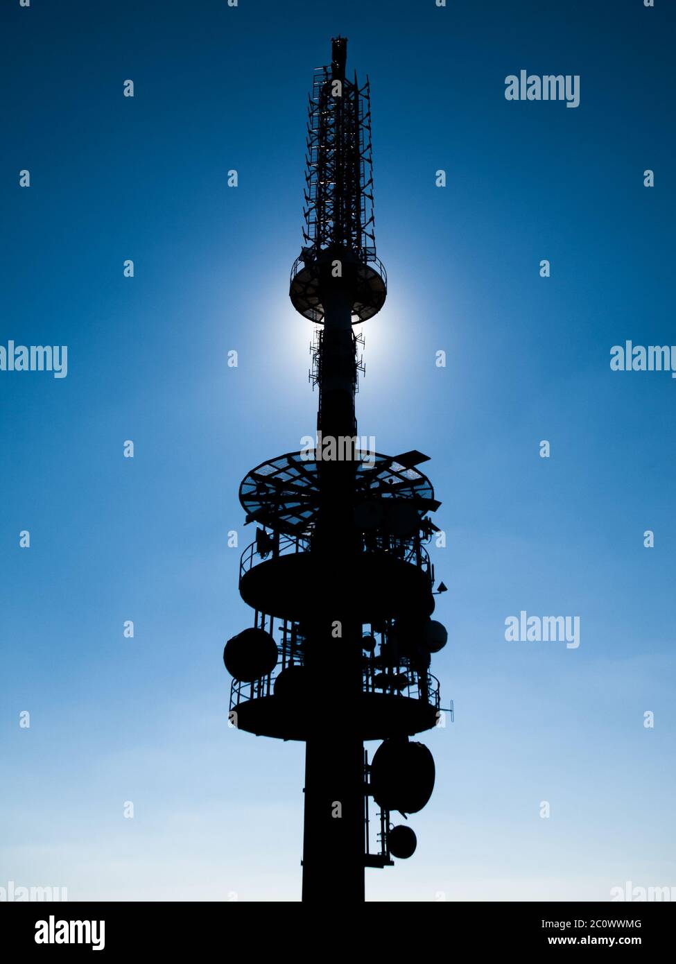 TV transmitte tower silhouette with sun hidden behind and blue sky background. Stock Photo