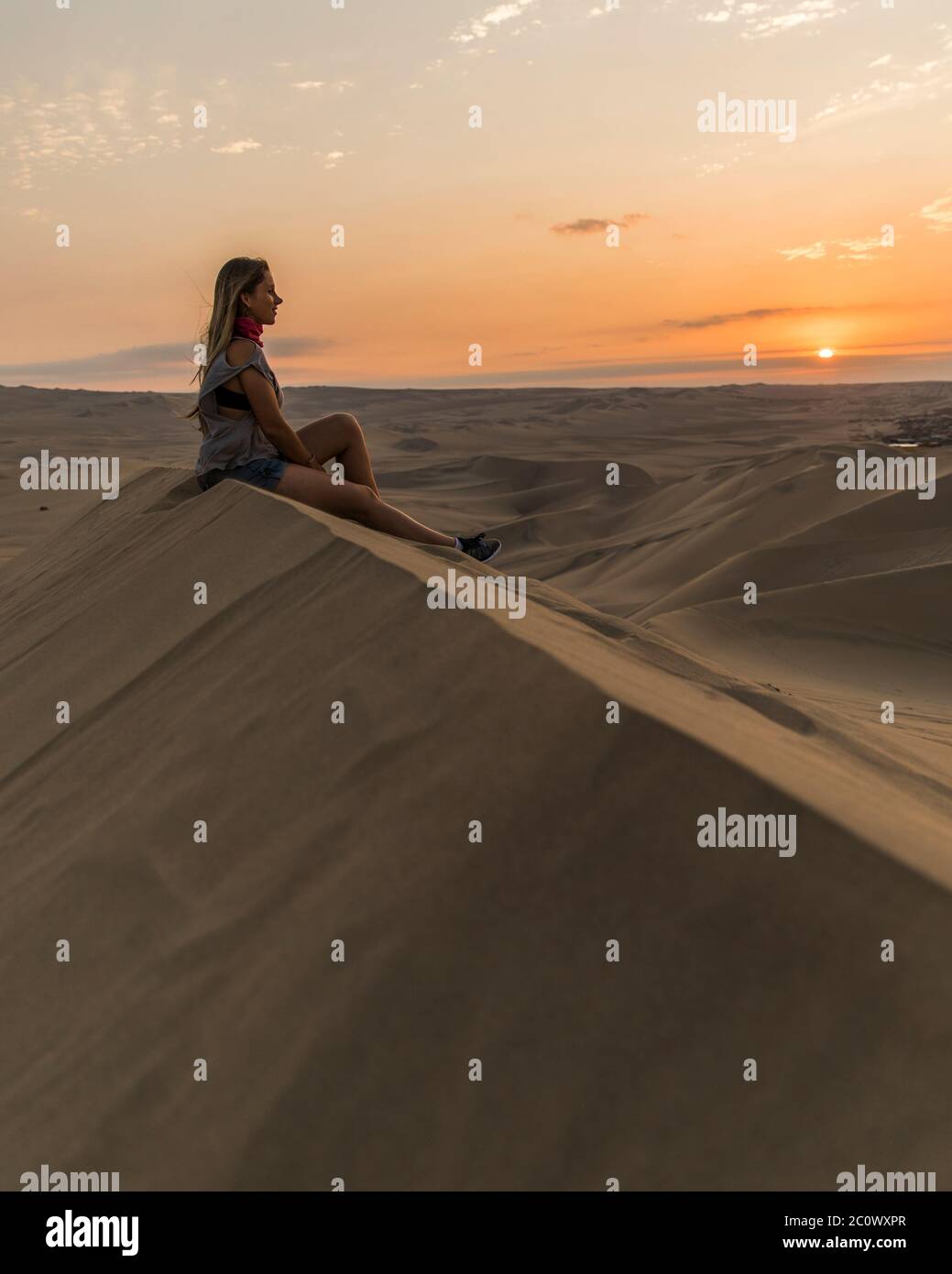 woman in the top of a dune in the middle of the desert, little clouds and sunset Stock Photo