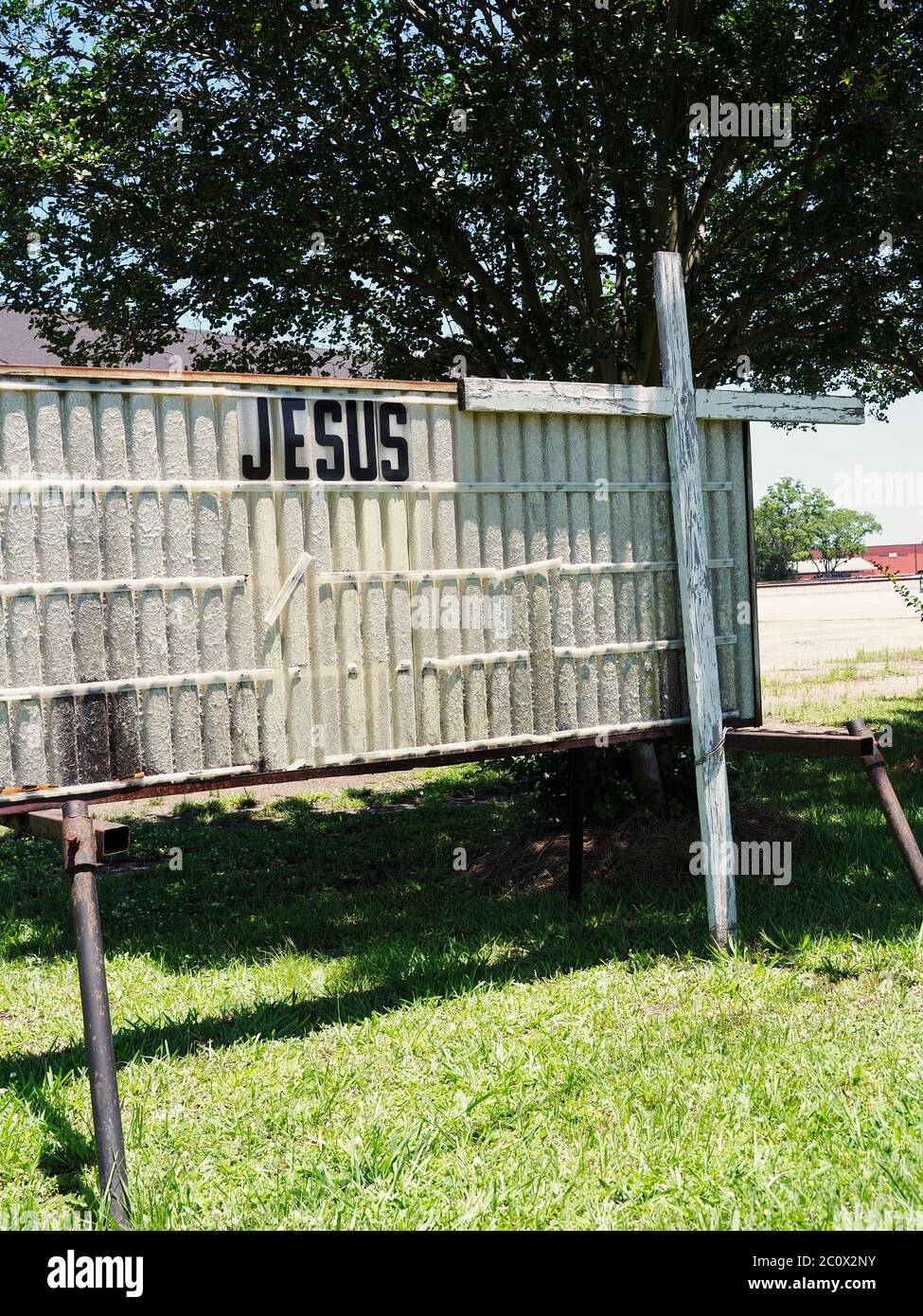 Old, aging and dilapidated church sign with the name Jesus displayed standing next to a white cross with peeling paint in Montgomery Alabama USA. Stock Photo
