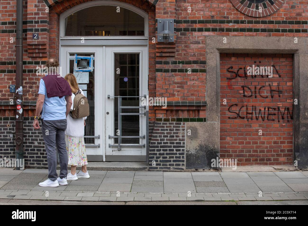 Hamburg, Germany. 12th June 2020. Picture shows a bride and groom walking past the vandalised exterior of the offices on Pickhuben in Hamburg belonging to Johann Schwenn law firm representing Christian Brueckner suspect in the disappearance of Madeleine McCann. 12th June 2020. Hamburg, Germany, Europe Stock Photo