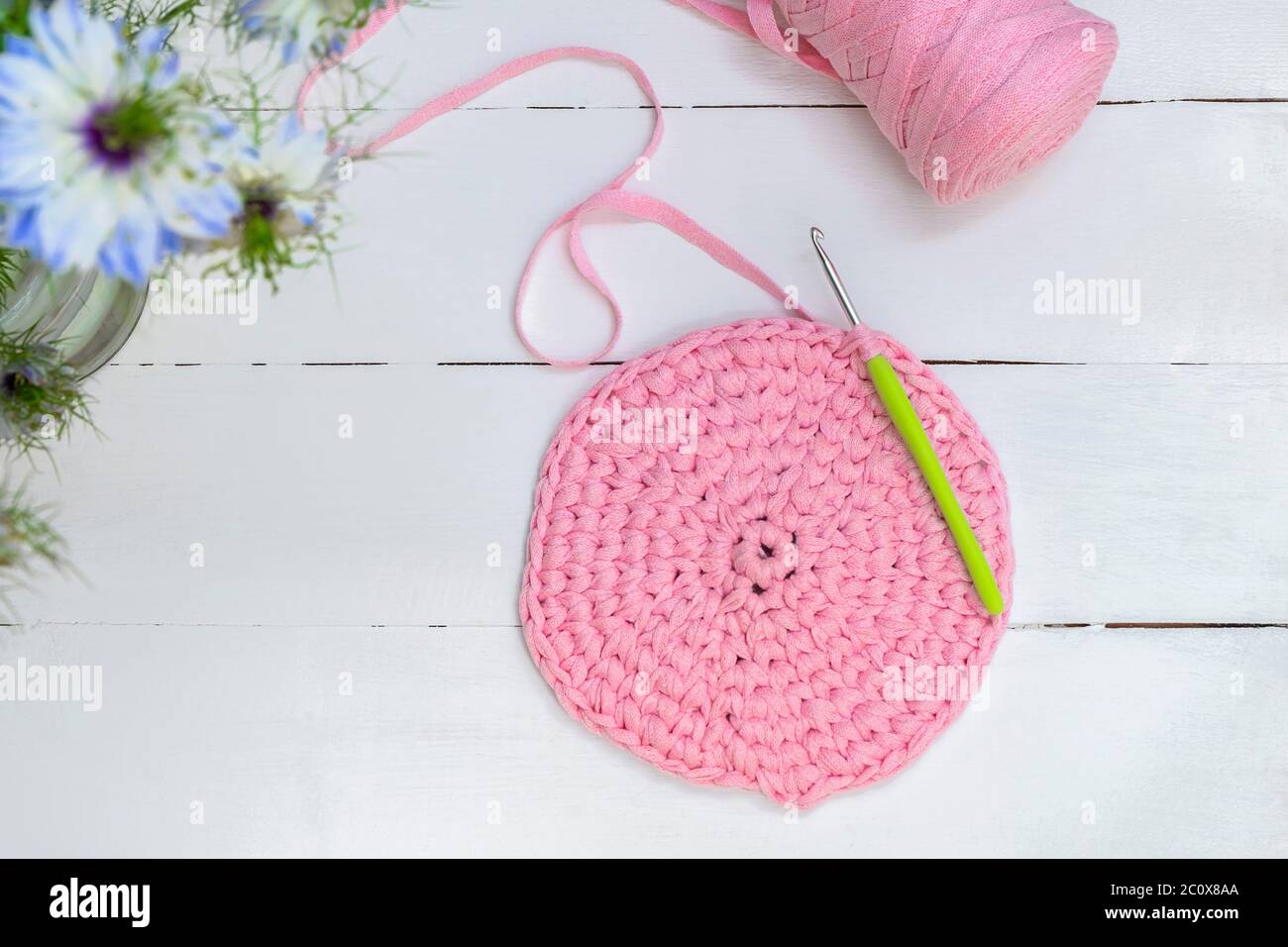 Crocheting and home hobby concept. Top view of crochet work with crochet hook and pink yarn on white wooden table Stock Photo