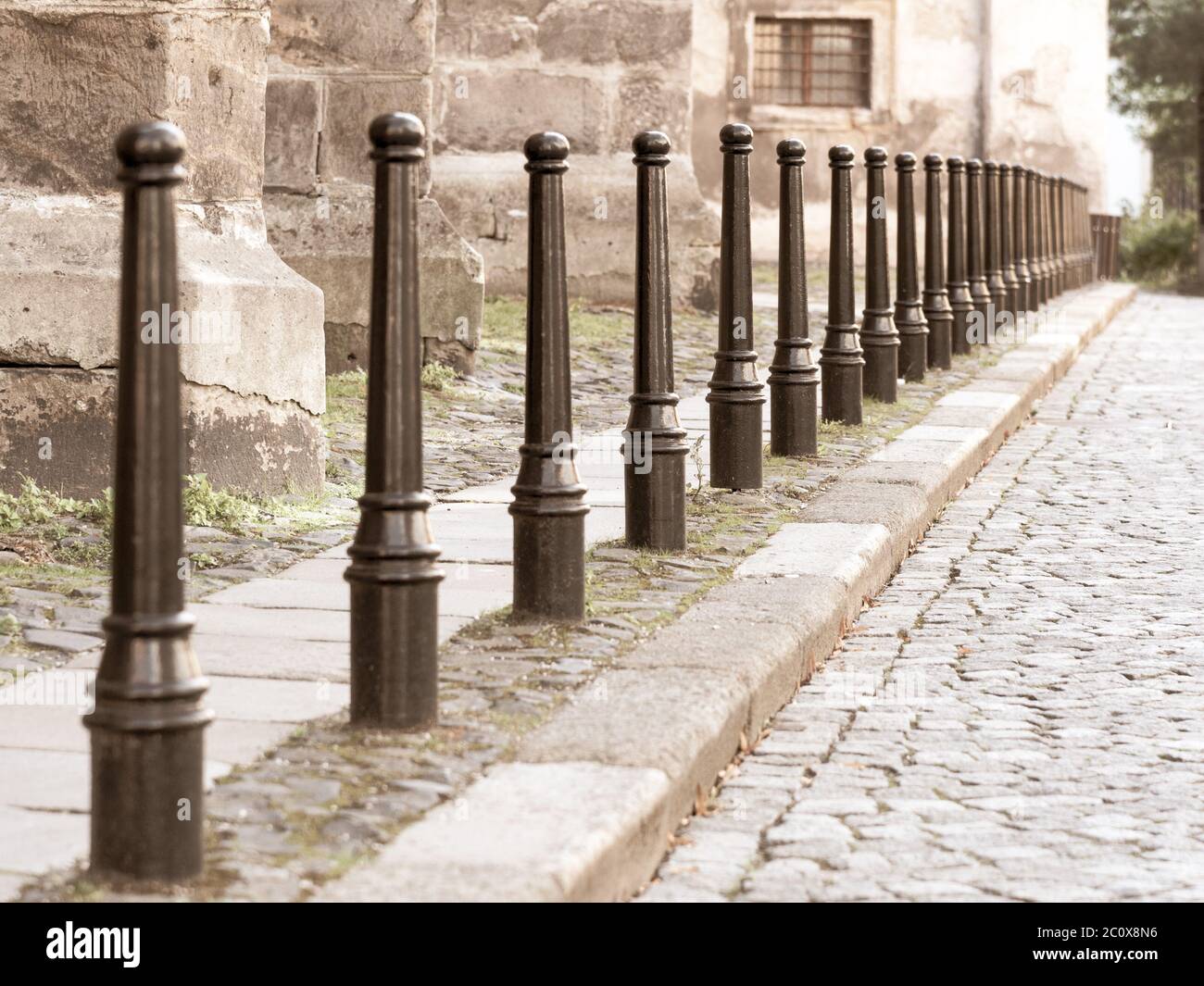 Row of iron pillars between cobbled street and pedestrian sidewalks. Stock Photo