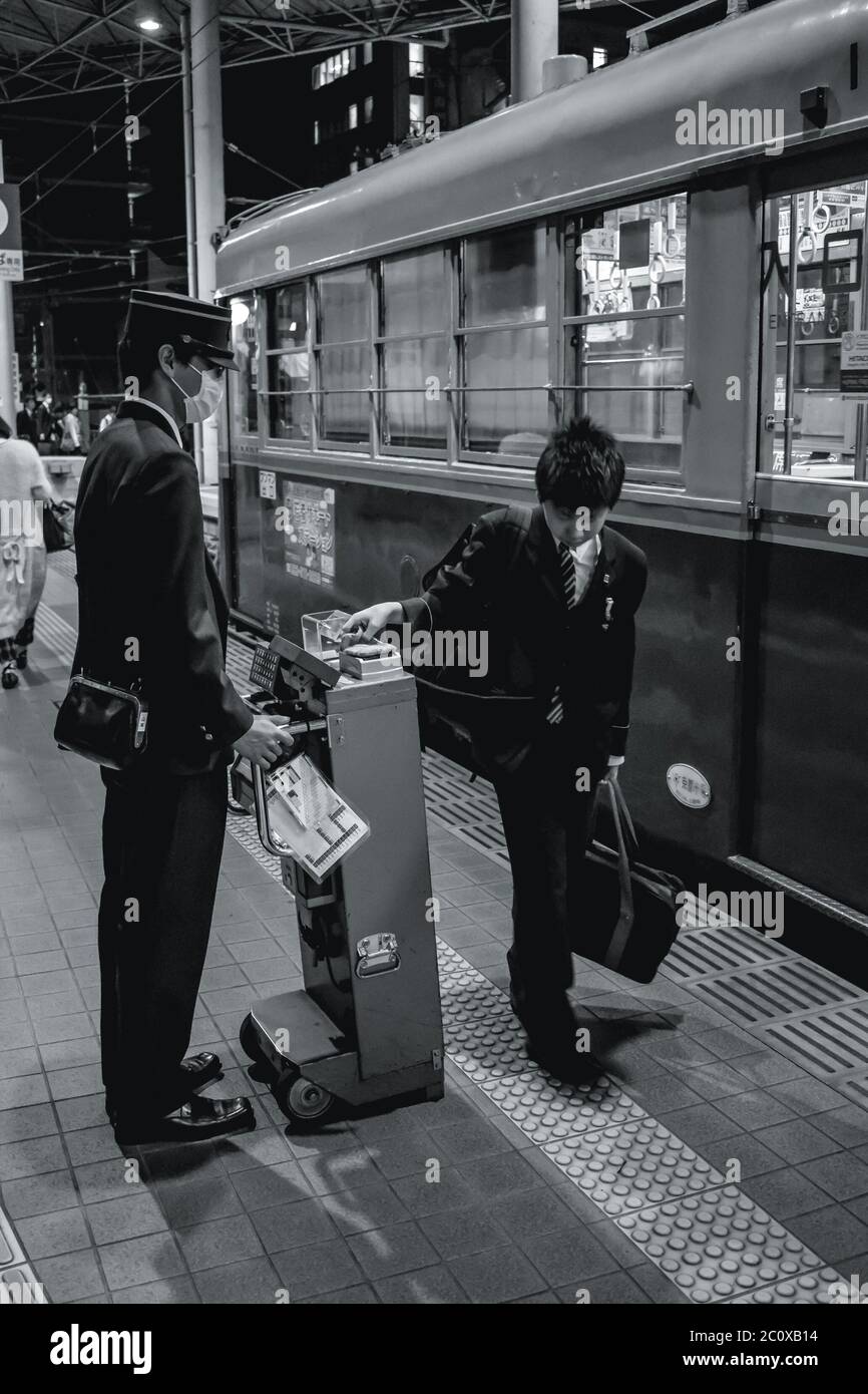 Controller controlling young mans tram tickets outside the tram in Hiroshima Japan Stock Photo