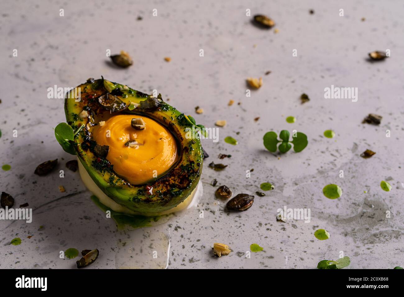 Avocado stuffed with eggs, tuna and sauce, arugula and dill on the black modern dish. Black cutlery, napkin and background. Keto diet healthy food. Stock Photo