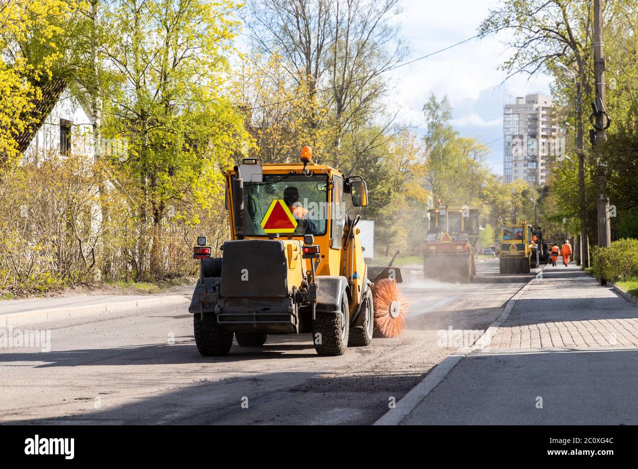 Tractor with spinning brush cleaning newly laid asphalt. Reconstruction and repair of a street road, municipal work. Stock Photo