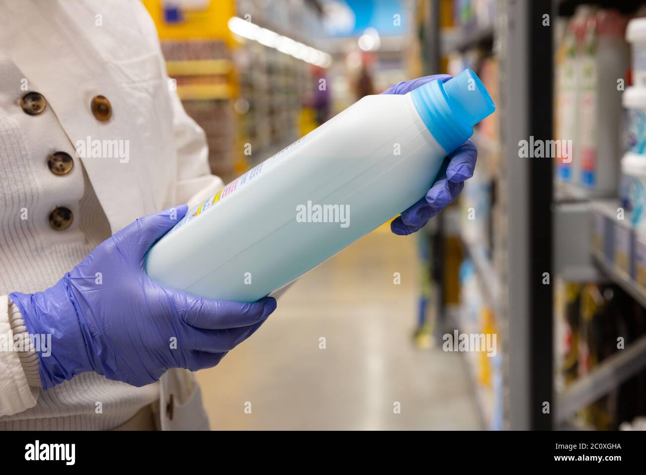 Woman wears rubber protective medical gloves, chooses household chemicals, disinfectant for home in supermarket, close up. Protective measures against Stock Photo