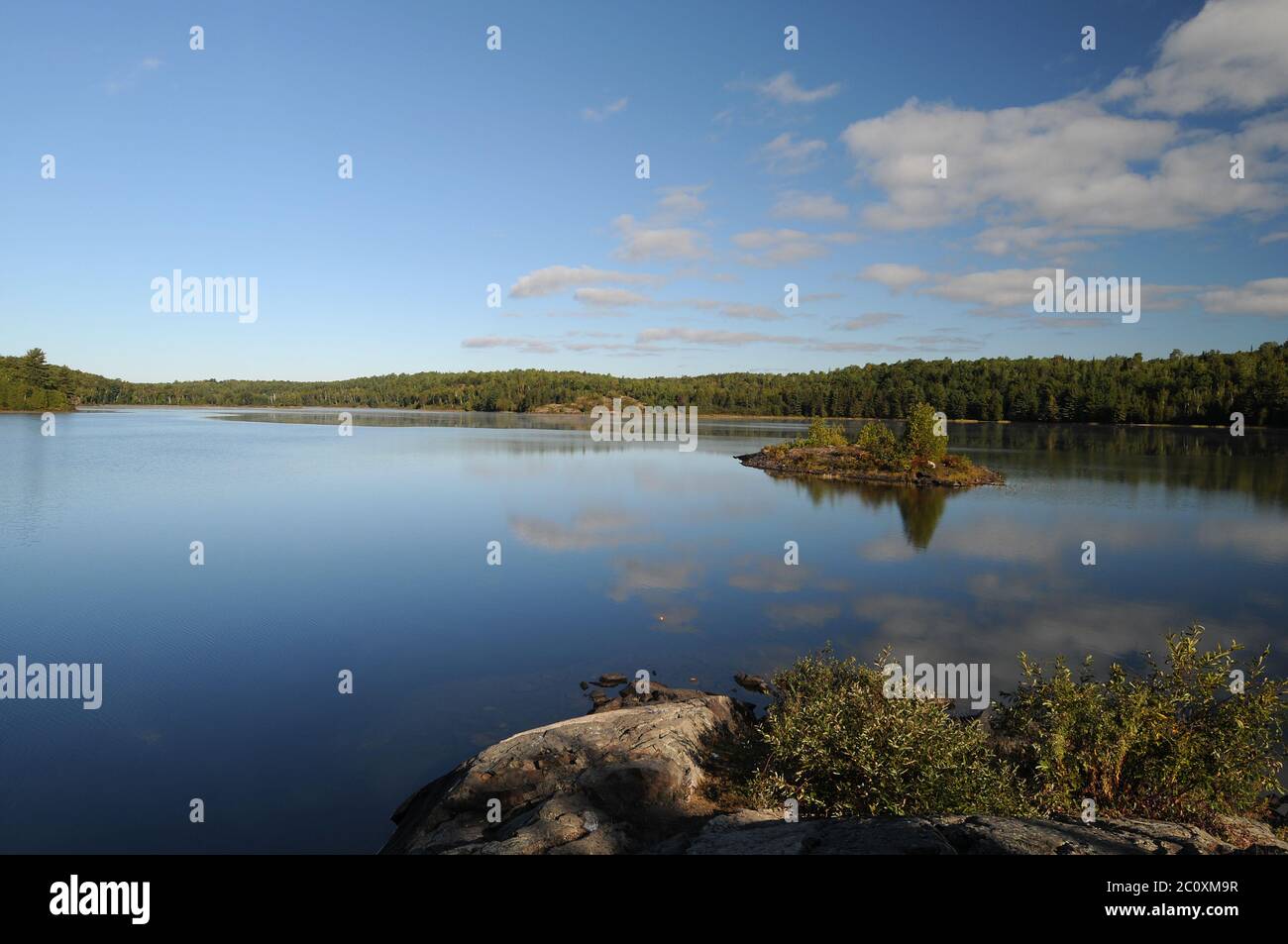 Summer scenery lake with blue sky and whit fluffy clouds reflection on the water displaying its summer season in a peaceful moment. Stock Photo
