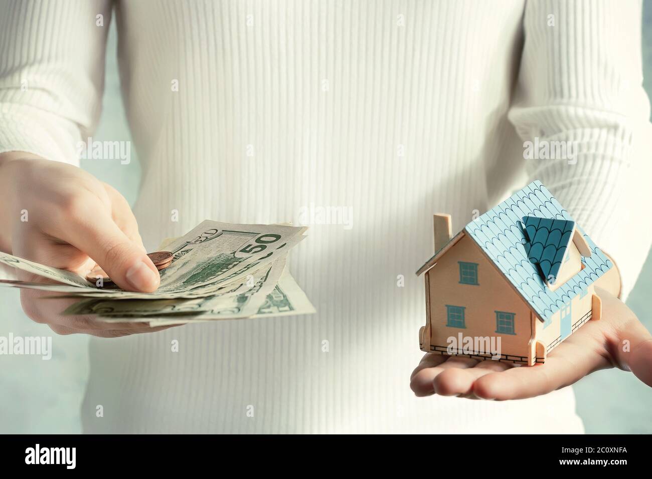 Real estate price and construction concept. Girl weighs money and a toy house in her hands. Stock Photo