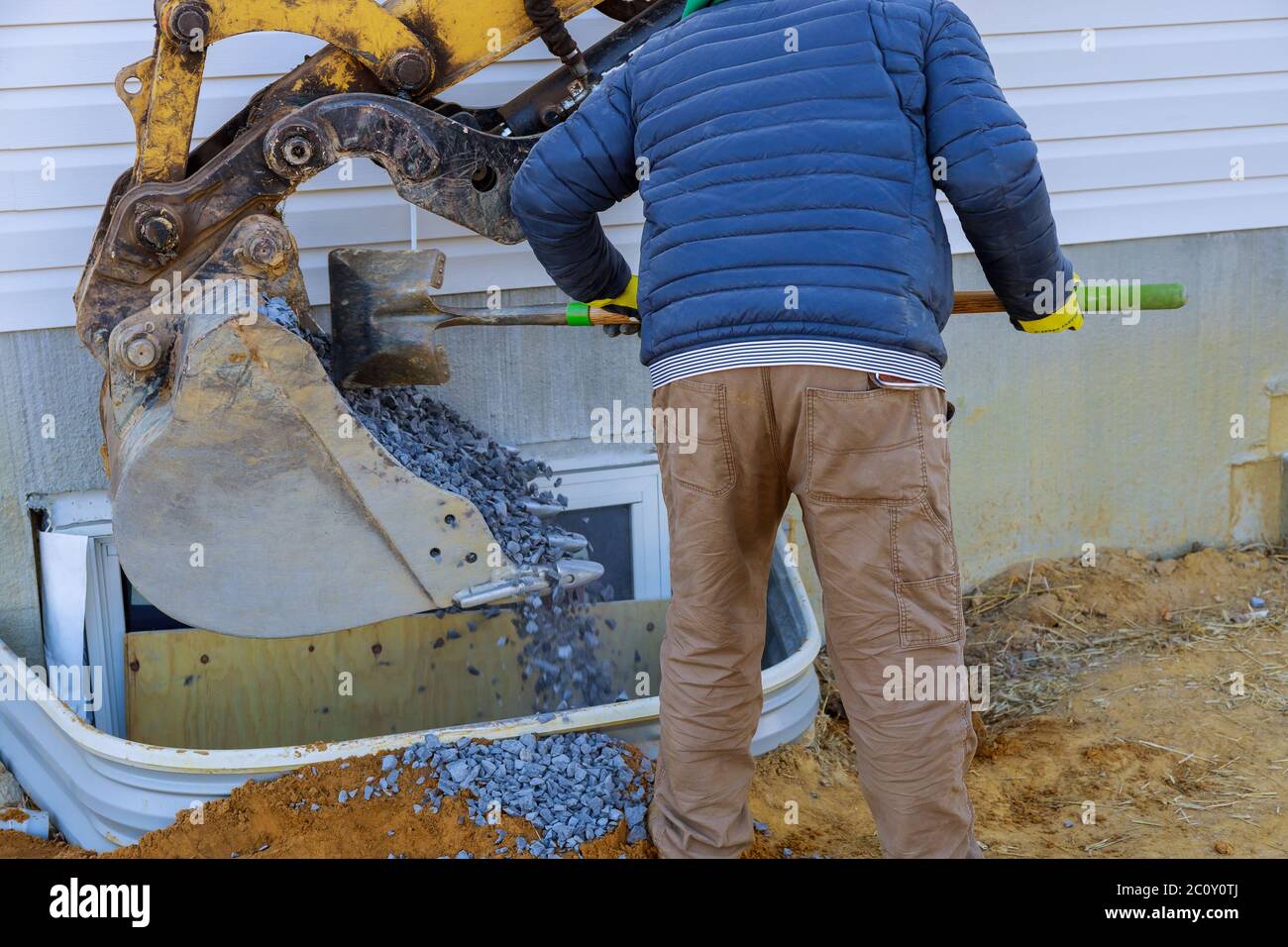 Bucket moving gravel in the window well on basement construction from