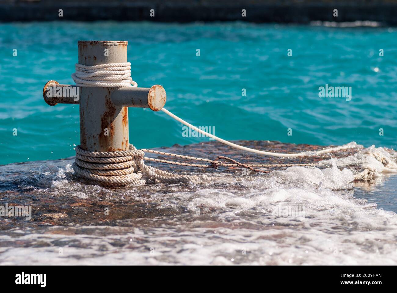 Rusty mooring bollard with ship ropes and  clear turquouse sea ocen water on background Stock Photo