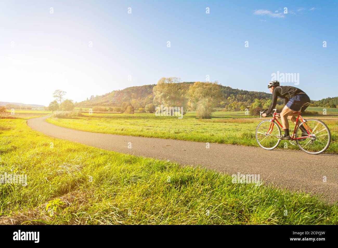 Cyclist on a racing bike in scenic autumn landscape riding into the sunset Stock Photo