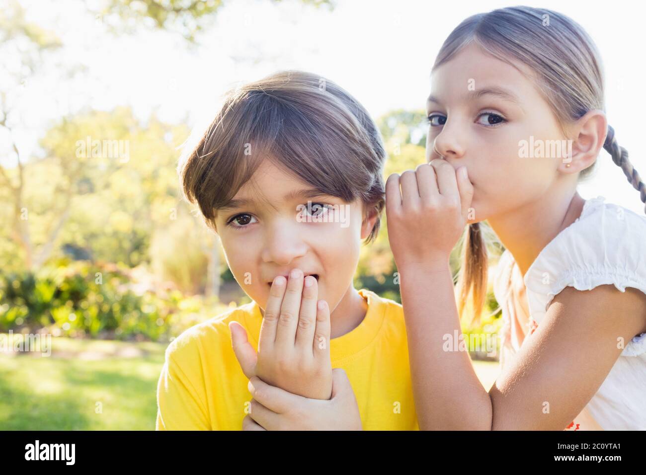 Girl telling a secret in the ear of a little boy Stock Photo