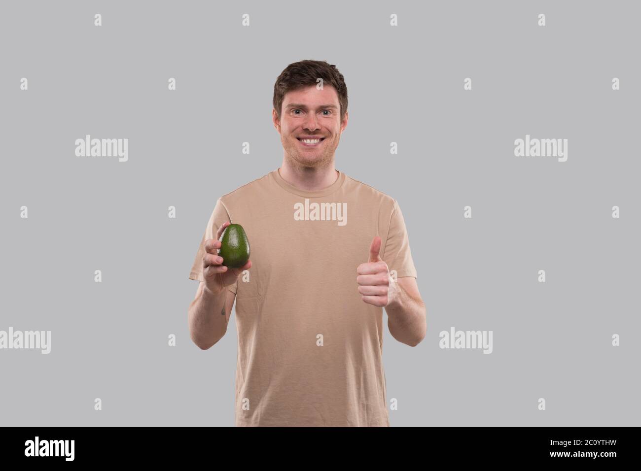 Man Holding Avocado and Thumb Up Isolated. Healthy Life, Eat Green Concept Stock Photo