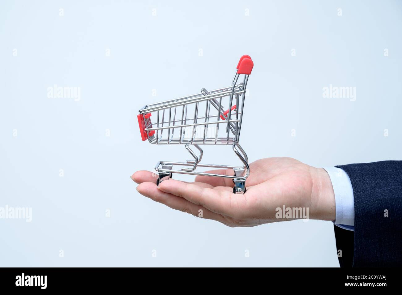 Man in suit holding small shopping trolley in hand. Close up. Business, commerce and shopping concept. Stock Photo