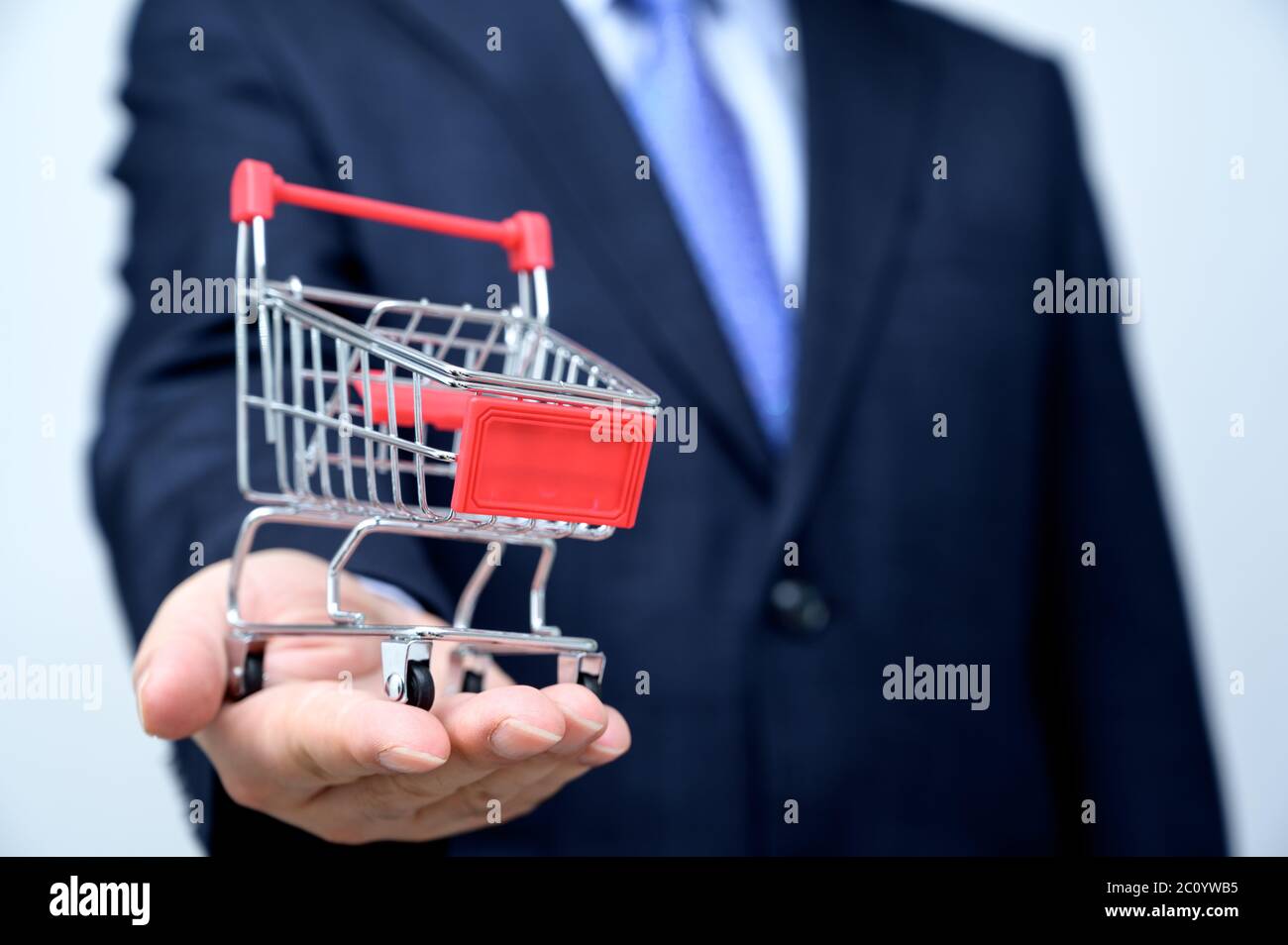 Man in suit holding small shopping trolley in hand. Close up. Business, commerce and shopping concept. Stock Photo
