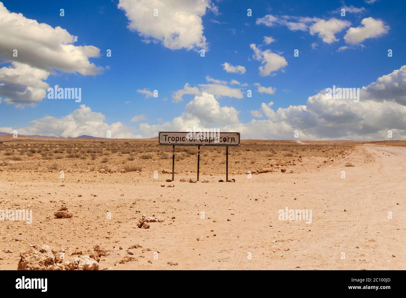 Tropic of Capricorn sign at a desert dirt road in Namibia under a blue sky with some clouds over the sand on a hot day. Stock Photo