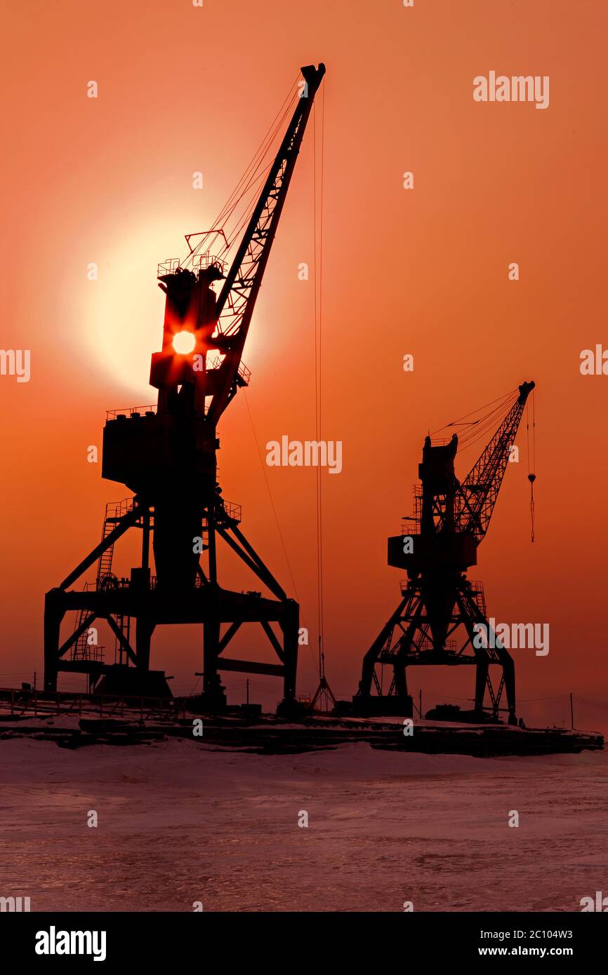 Silhouettes cranes freight ship on shore of Lake Baikal in winter at sunset. Stock Photo