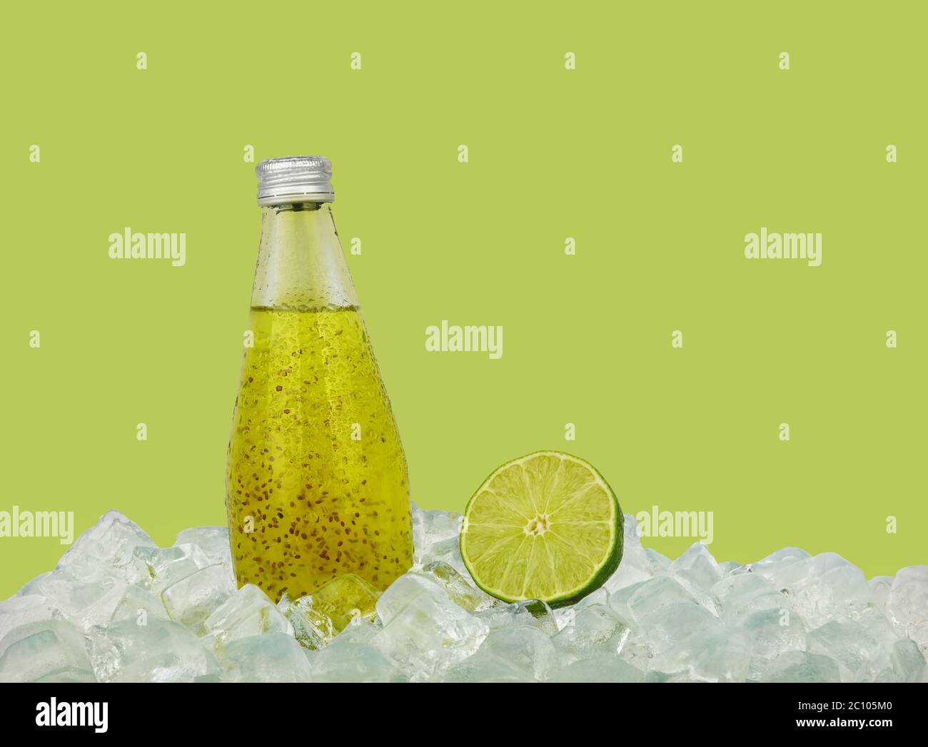 Close up one glass bottle of cold juice cocktail drink with chia seeds and half cut lime on ice cubes isolated on green background, low angle side vie Stock Photo