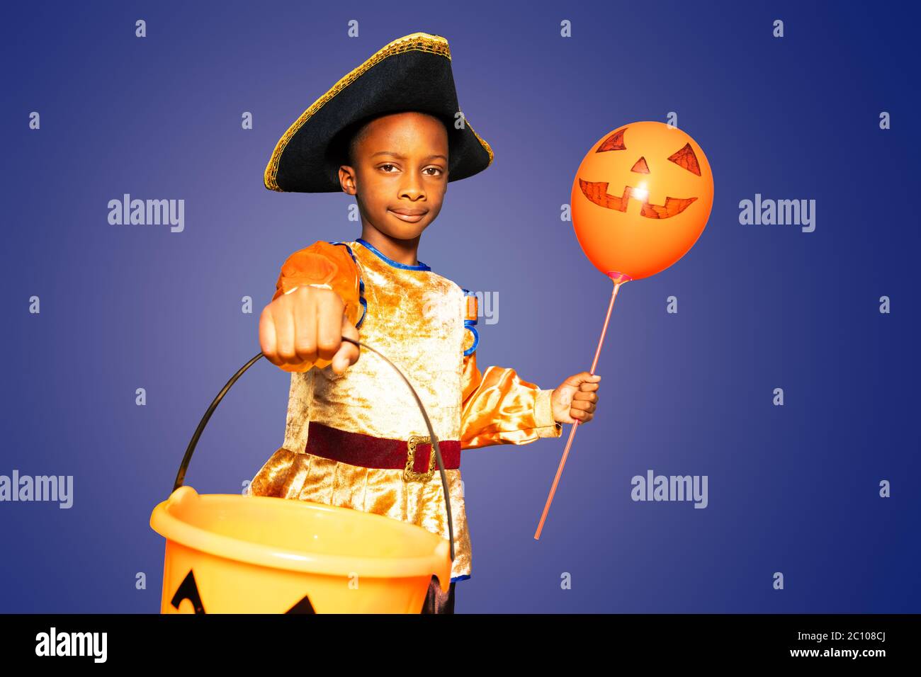 Serious portrait of a little boy with scary bucket for candies and in Halloween costume holding orange balloon Stock Photo