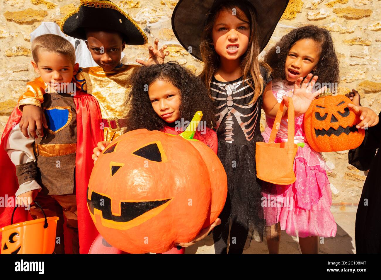 Group of cute little kids in costume with girl hold huge orange pumpkin Halloween Stock Photo