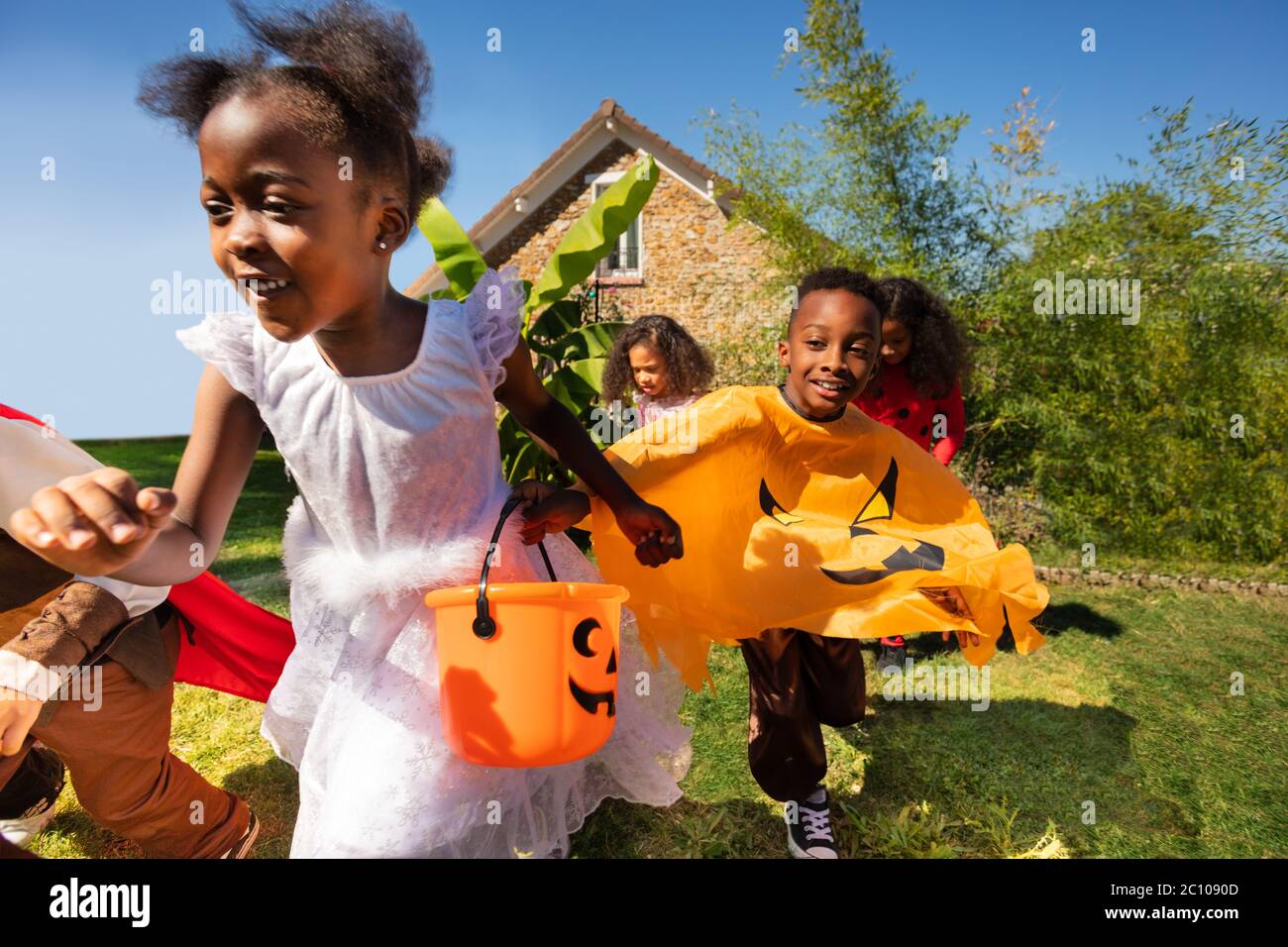 Close portrait of a group of little children run in Halloween costume on the lawn before the house holding hands Stock Photo