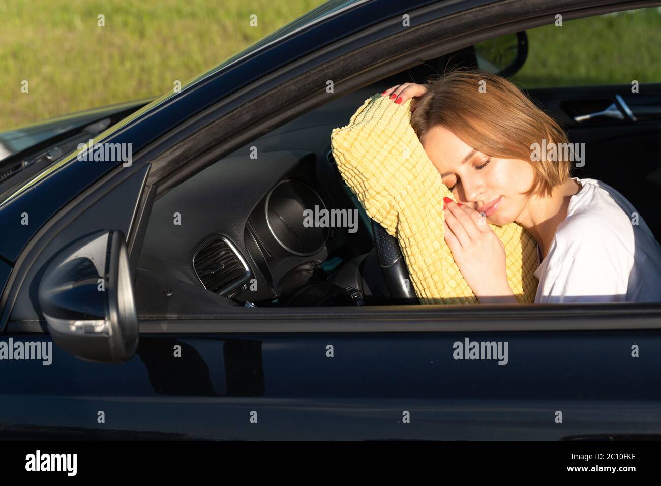 Tired young woman driver asleep on pillow on steering wheel, resting after long hours driving a car. Fatigue. Sleep deprivation. Stock Photo