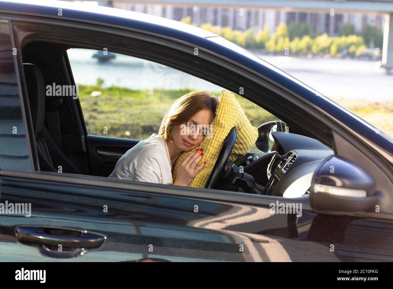 Tired young woman driver asleep on pillow on steering wheel, resting after long hours driving a car. Fatigue. Sleep deprivation. Stock Photo