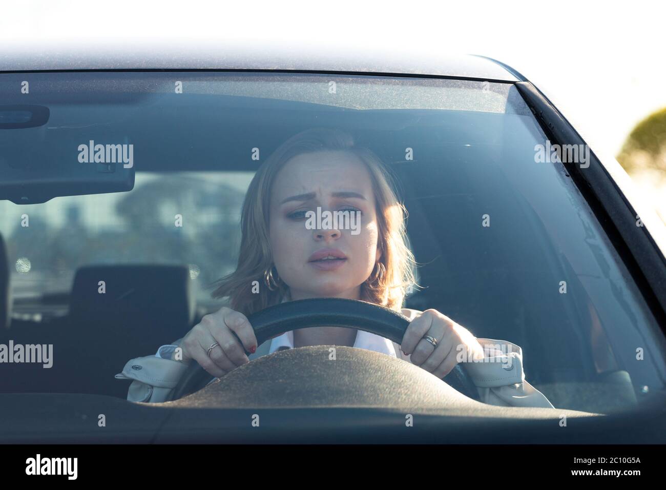 Woman drives her car for the first time, tries to avoid a car accident, is very nervous and scared, worries, clings tightly to the wheel. Stock Photo