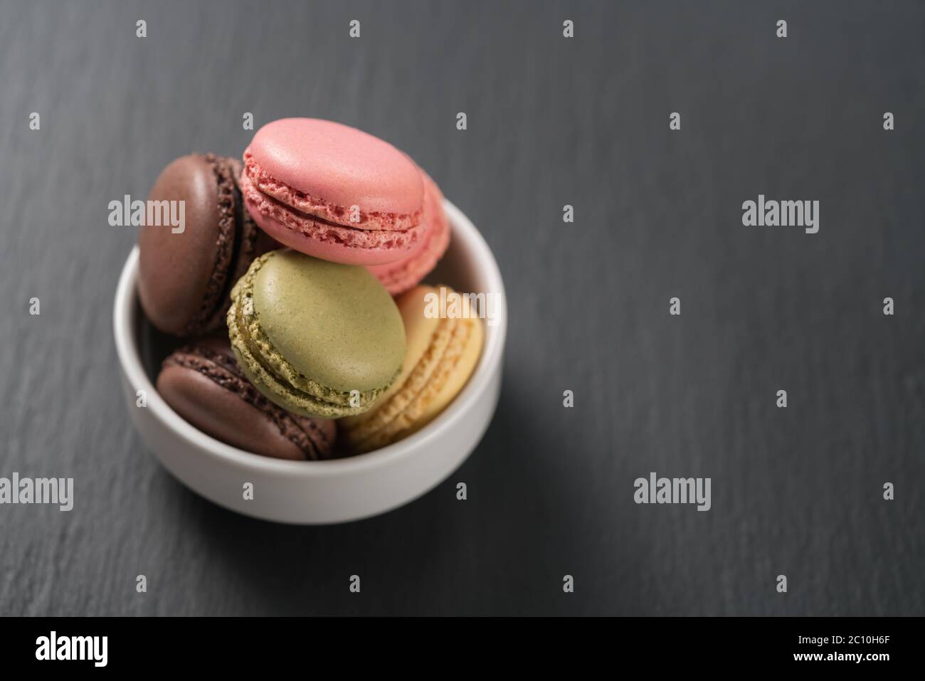 assorted macarons in white bowl on slate background with copy space Stock Photo