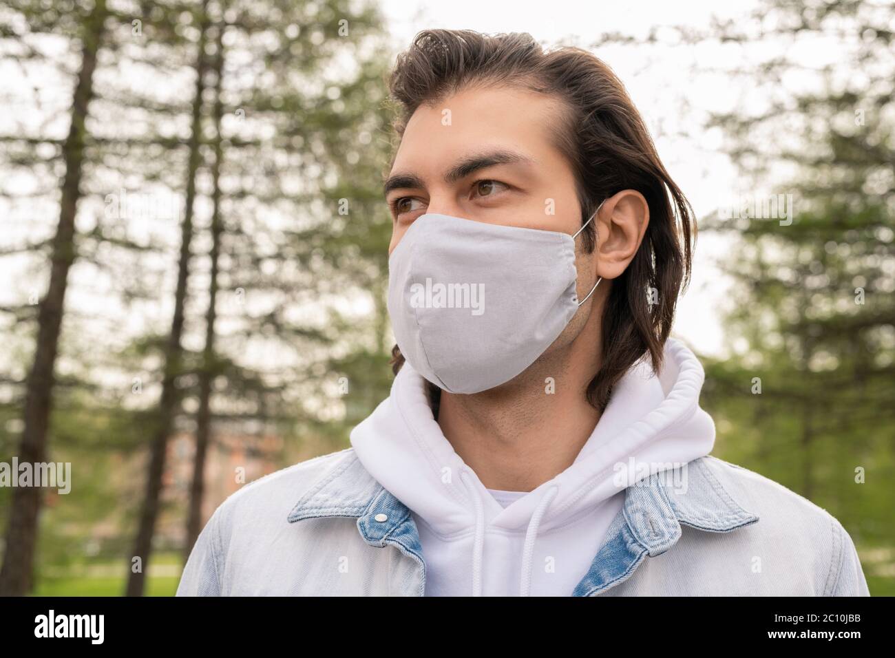 Handsome middle-aged man in cloth mask looking around while walking in forest during coronavirus pandemic Stock Photo
