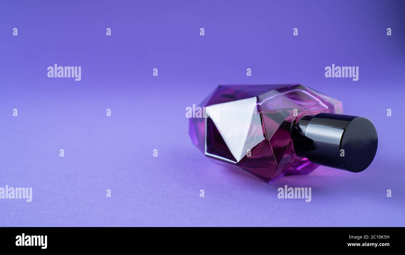 Fashion perfume in glass bottle on purple background. Heart bottle shape. Red bottle. Passionate perfume. Isolated Stock Photo