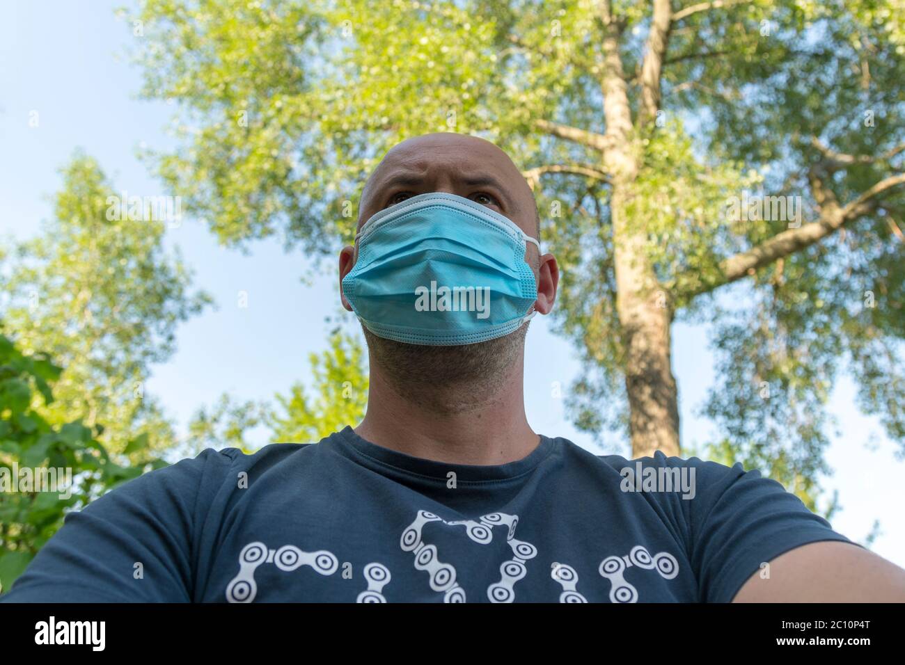 Portrait of young man wearing medical mask posing in sunny park. Close ...