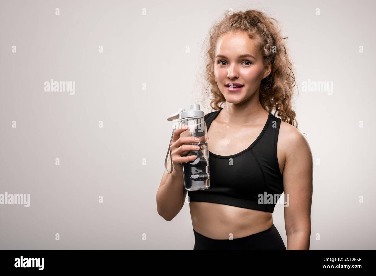 Happy young sportswoman in black activewear going to drink water from ...