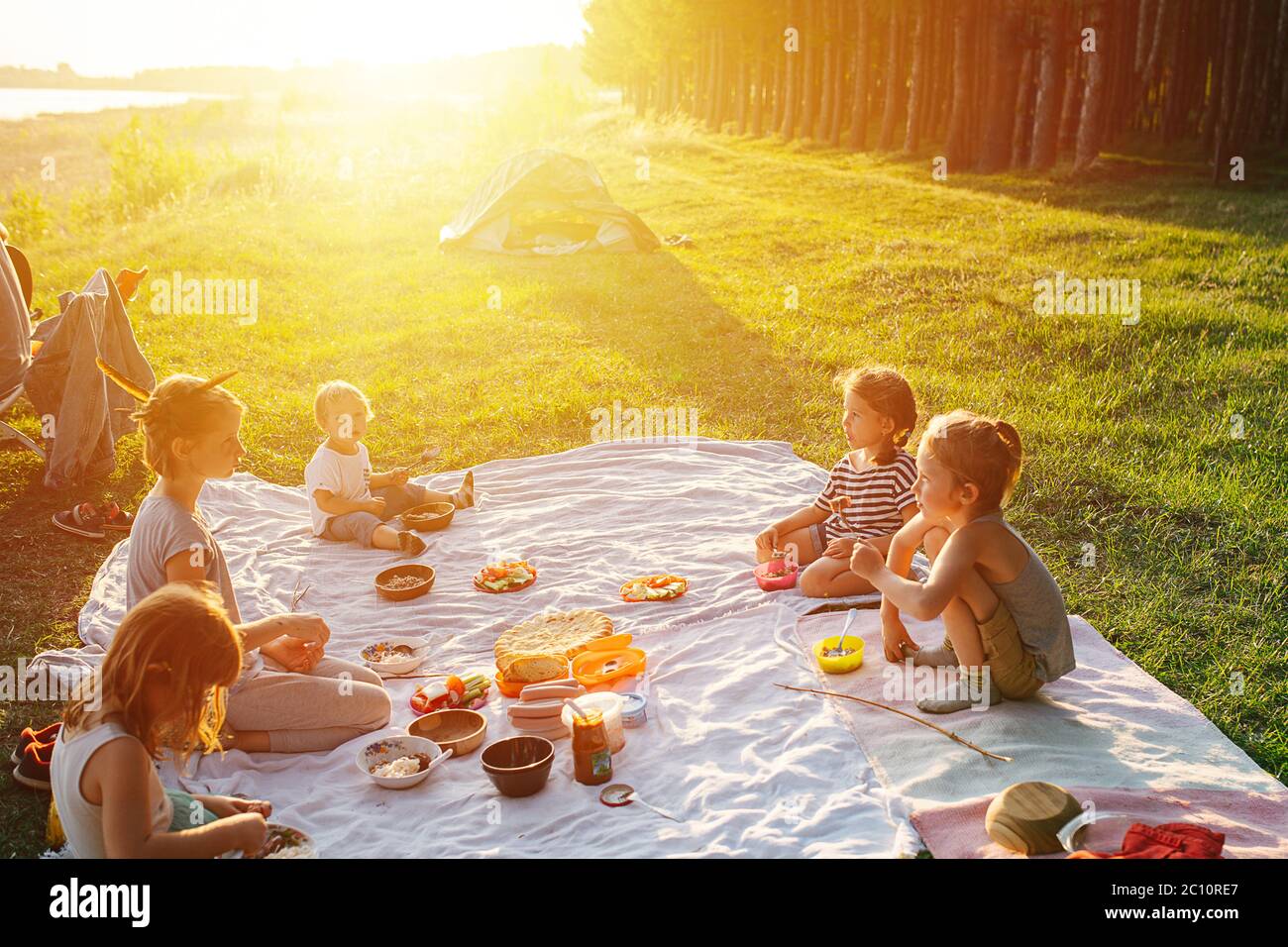 Kids having picnic on a lawn, lighted with a beautiful setting sun. Stock Photo
