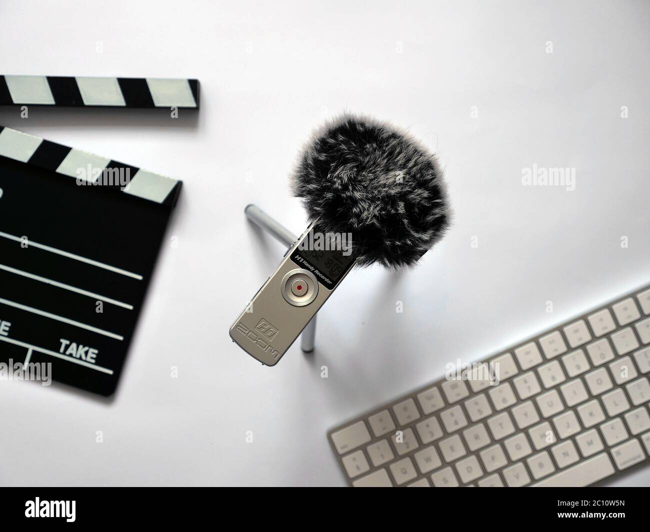 Record audio inside on zoom h1 recorder with dead cat in recording studio  on white background in natural daylight. The background shows objects such  as Clapperboard and keyboard. You can use this