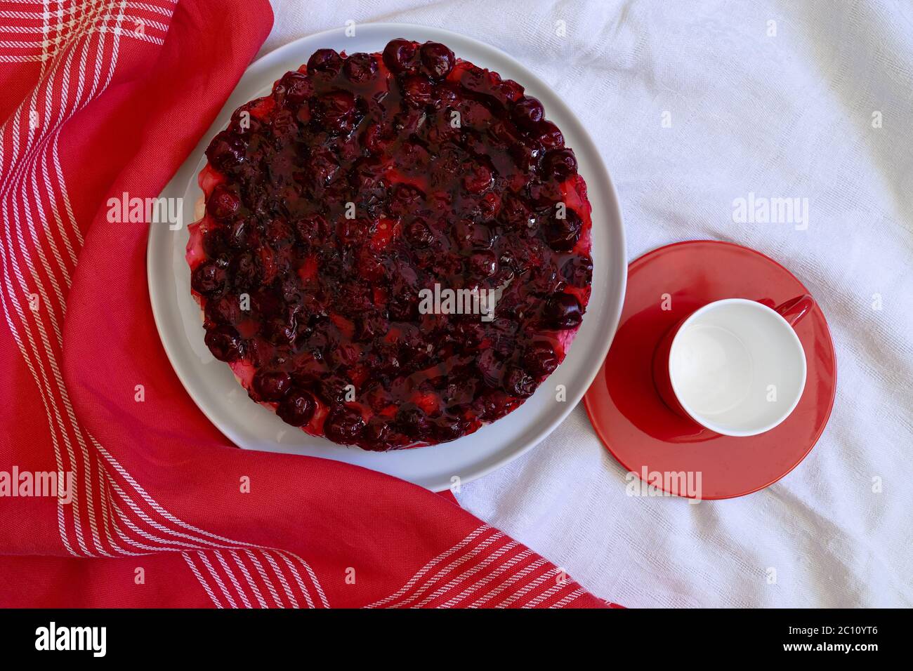Homemade no baked cake with mascarpone cheese cream, fresh cherries and jelly  on a white plate,  red small plate and empty cup Stock Photo