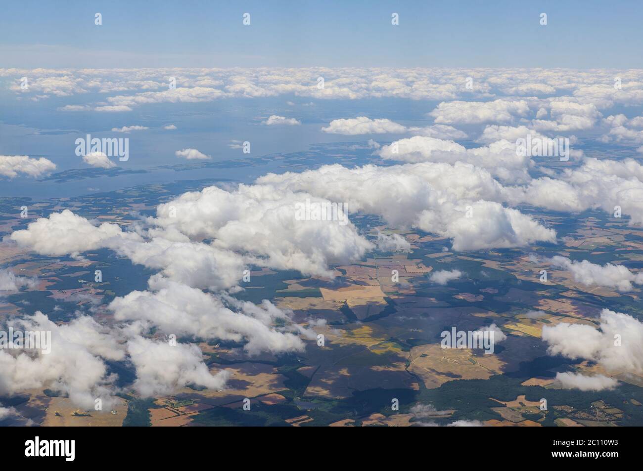 Airplane flying above clouds over beautiful green grass fields land above is the blue sky Stock Photo