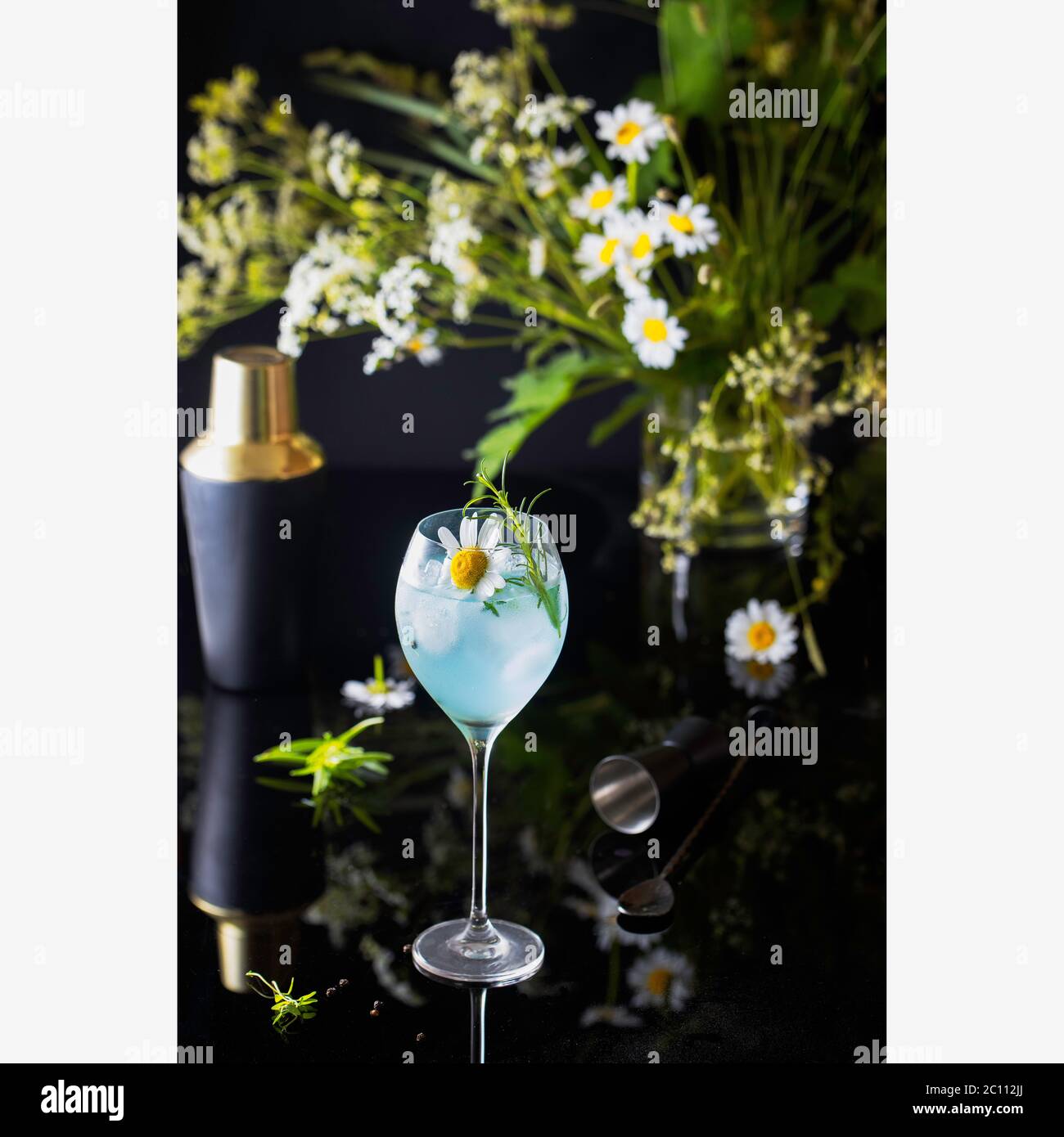 Blue gin in a tall glass covered by water droplets with summer daisy flowers as a garnish and on