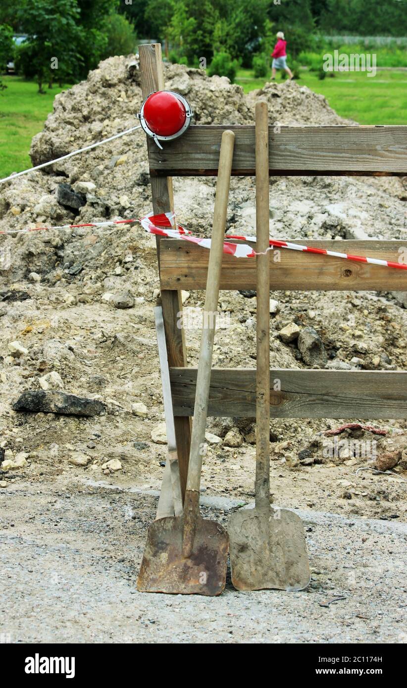 two shovels, a red lamp to the fence, enclosing ditch buried in the ground. Stock Photo